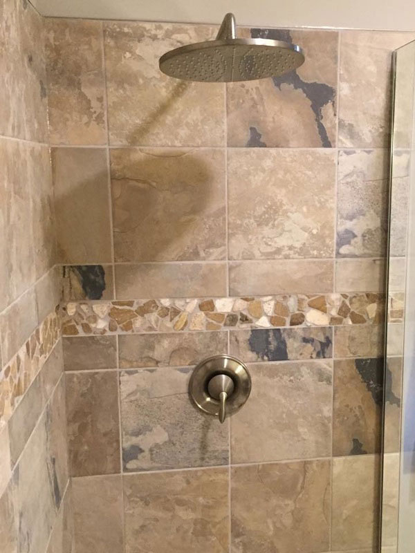 detail view of river rock accent strip surrounded by beige and brown large ceramic tiles in shower