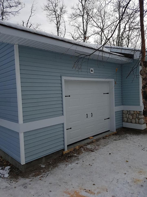 Attached single car garage viewed from side with light blue siding and white overhead door