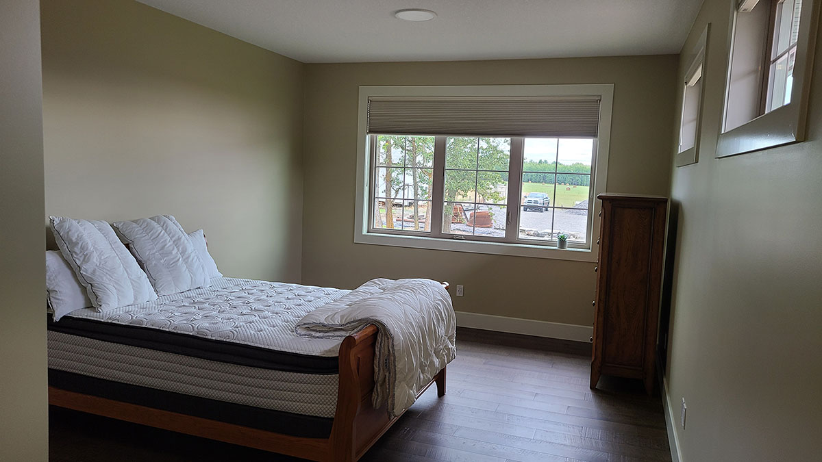 Bedroom with bed, dresser and large windows and hardwood flooring