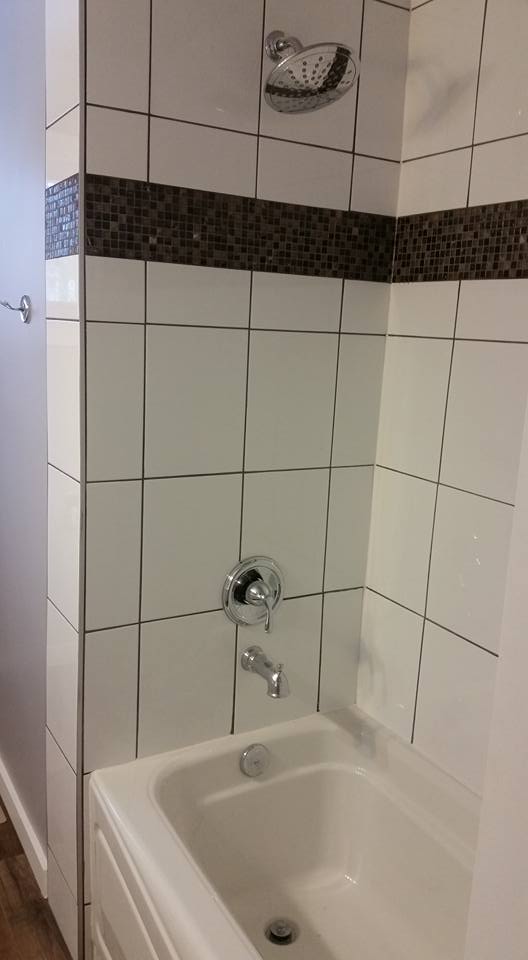white tile with dark mosaic tile band over a white bath tub