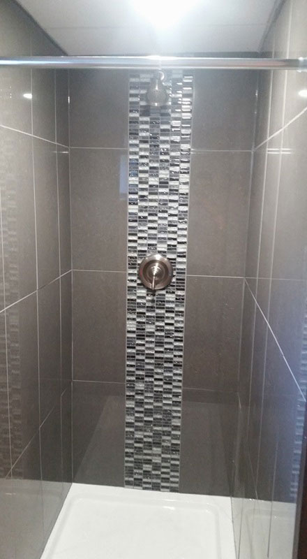 Large grey tiles of this shower are accented by a panel of glass mosaic tiles