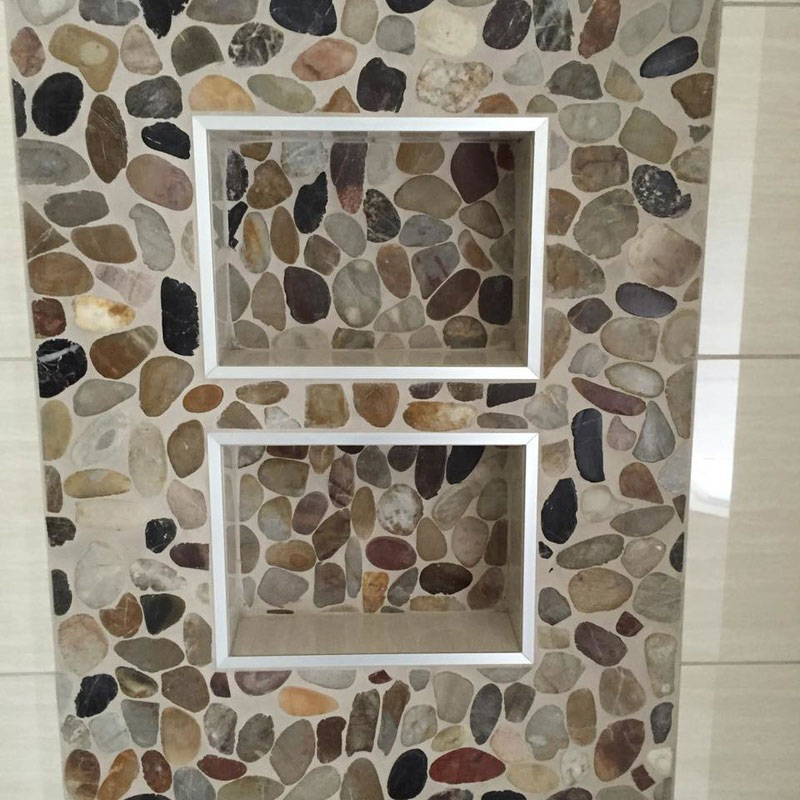 Close-up view of pebble accent niches set in pebble panel of shower