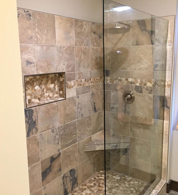 Shower with glass panel, rain shower head, shampoo niche and shaving shelf done in warm beige tones with river rock accents