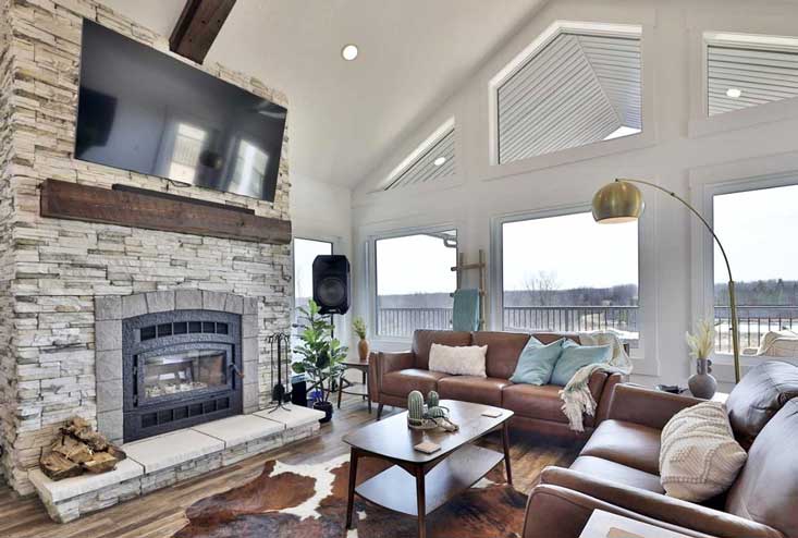 Living room with leather couches and large stacked stone fireplace has vaulted ceiling and large windows