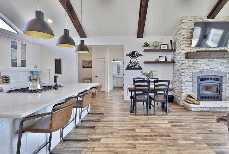 White kitchen view into open plan dining room with exposed beams overhead and fireplace to right